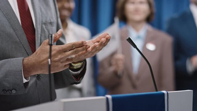 Close-up shot of hands of unrecognizable male Indian or Asian candidate in grey suit, red tie gesticulating while speaking convention - clasping, interlacing fingers, counting his propositions