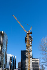 High rise cityscape of a modern downtown, tall crane and construction of a new skyscraper on a sunny blue sky day
