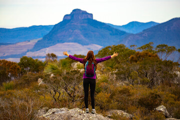 Naklejka na ściany i meble backpacker girl celebrating successful hike to the summit of mount maroon; rock scrambling in mount barney national park, queensland, australia