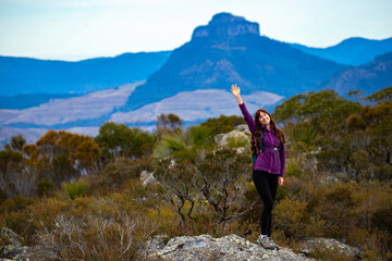 Naklejka premium backpacker girl celebrating successful hike to the summit of mount maroon; rock scrambling in mount barney national park, queensland, australia