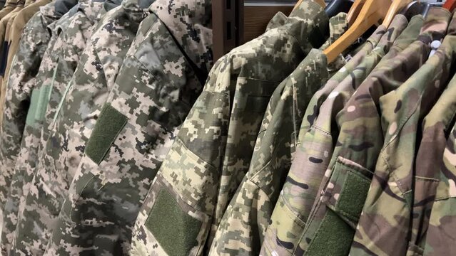 Military camouflage uniforms  in a variety of colors and patterns hanging on a racks in a store.