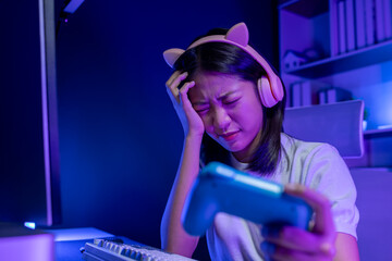 A young Asian woman is playing a game in a private room, stressed out because the game situation is tense because her team is about to lose, Try hard to win the game.