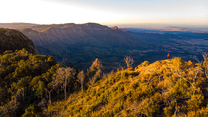 aerial view of hiker girl standing at the top of mountain, enjoying sunset over unique, folded mountains in south east queensland, australia; main range national park near brisbane, bare rock lookout	