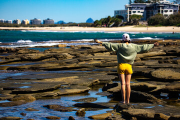 pretty girl enjoying a sunny day on the beach in caloundra, sunshine coast, queensland, australia; exploring rock pools on the shore of pacific ocean near brisbane
