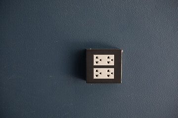 Black power socket mounted on dark gray wall.