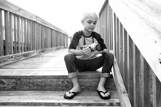 Black and white casual portrait of a child sitting on stairs admiring his camera on a bright sunny day