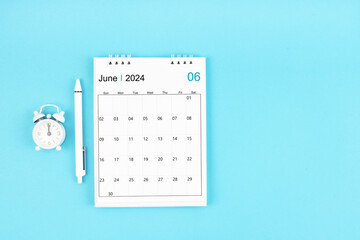 June 2024, Monthly desk calendar for 2024 year and pen with alarm clock on blue background.