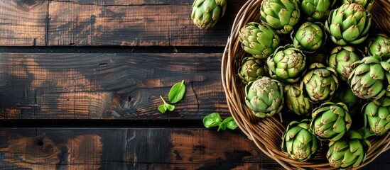 A wicker basket filled with fresh green artichokes rests on top of a wooden table. The vibrant green of the artichokes contrasts beautifully with the natural brown of the wood. - obrazy, fototapety, plakaty