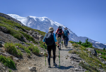 Three people hiking Sunrise Trail in summer. Snow-capped Mount Rainier looming large in front....