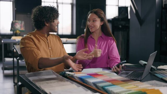 Multiracial couple creative designers work in modern office studio Arabian Indian man Caucasian woman using phone choosing perfect sample of material color tone for new house interior design project