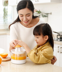 Asian mother teaches daughter to make fresh squeezed orange juice in kitchen