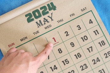 Hand pointing on May 1 2024 date on calendar flat lay in blue background. Labor day or...