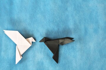 White dove and black rave paper origami in blue background. Good and evil, face fear and opposite attraction concept. 