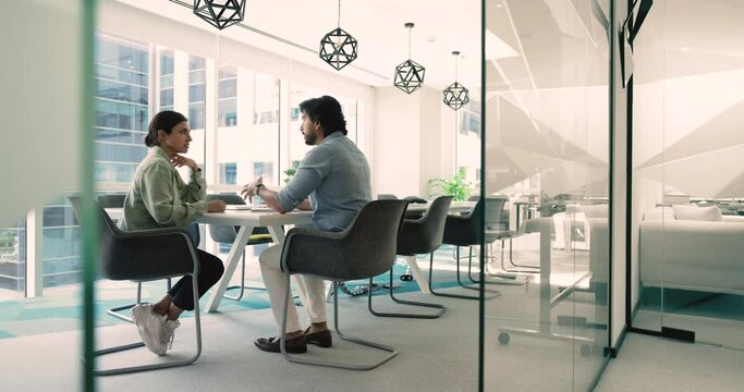 Indian businesspeople met in modern conference room sit at desk discuss project details, to solve issues, share opinion, working on collaborative task, sales manager makes commercial offer to client