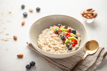 Oatmeal porridge with fruit and berries in bowl on the table. Homemade healthy breakfast cereal with strawberry, kiwi fruits, blueberry and almond
