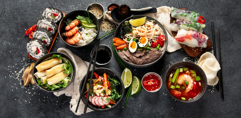 Traditional Asian food table. Spring roll, rice, shrimp, sushi, vegetables, meat on dark background