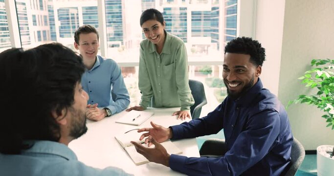 African male employee gives high five teammate, sit at desk take part in group briefing in modern boardroom. Gesture as effective teamwork, great work result and team spirit, make good deal, agreement