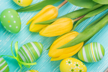 Easter eggs and yellow tulips on blue wooden table, top view