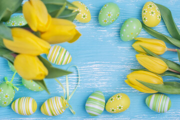 Easter eggs and yellow tulips on blue wooden table, top view