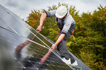 Man installer mounting photovoltaic solar panels on roof of house. Engineer in helmet installing...