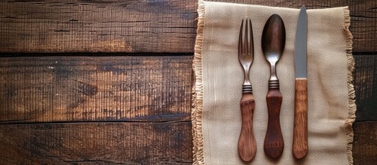 A knife, fork, and spoon rest neatly on a crisp white napkin on a wooden table, creating a simple and elegant dining setting.
