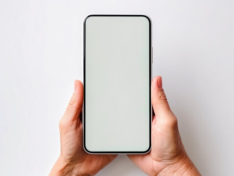 Hands or palms of an elderly woman holding smartphone with white screen with space for graphics, text or logo, top view from the eyes, isolated on light background. 