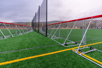 Portable softball baseball outfield fence with red fence cap on a synthetic turf football 