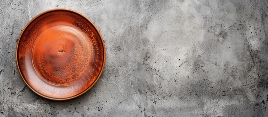 An attractive brown ceramic plate is placed on top of a grey cement wall, creating a contrast in textures. The plate is ideal for serving food and adds a touch of elegance to the otherwise plain wall.