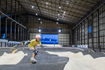 Fototapeta premium surfskate by asian child skater or kid girl fun playing skateboard or ride surf skate in pump track at skate park by extreme sports surfing to wears helmet elbow pads wrist knee guard for body safety