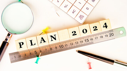 PLAN 2024 on wooden cubes along the ruler, next to a magnifying glass, calculator, paper clips, pen