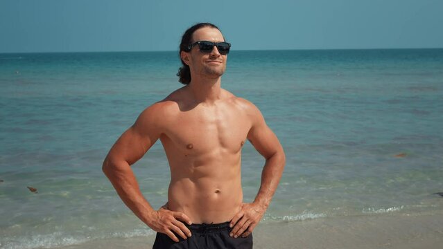 Hot man with muscular body stands on beach posing for camera. Amidst beach vacation vibes hot man embodies healthy lifestyle and allure of muscular body radiating confidence and charm hot man.
