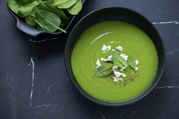 Bowl of freshly made spinach cream-soup on a black marble background, horizontal shot, elevated view