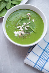 Bowl of spinach soup topped with feta cheese, vertical shot on a light-grey granite background, selective focus