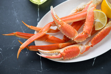 White plate with boiled crab claws and legs, horizontal shot on a black marble surface, middle close-up, selective focus