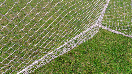 A woven net on a football goal. A football field with natural green grass. Playing football. A football field in summer. Mowed lawn for playing football