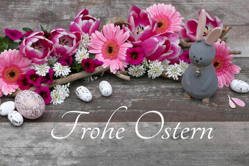Blumen Arrangement mit rosa  Ostereiern auf schäbigen Holzbrett mit dem Text Frohe Ostern.	