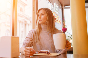 Woman with blonde hair sips cappuccino in a cafe. She is holding the glass up to her face, taking a...