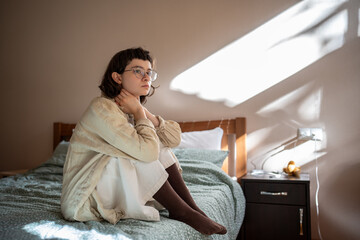 Melancholic lonely teen girl sits on bed, sadly looking at window, feeling anxiety depression....