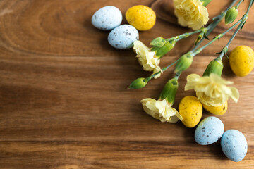 Yellow flowers and pastel yellow and blue colored eggs on a background of brown wood. Layout. Mockups. Springs background. Easter background. Easter eggs close up
