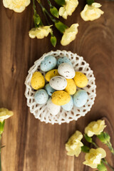 Yellow flowers and pastel yellow and blue colored eggs in a white small wicker basket on a background of brown wood. Layout. Mockups. Pastel Springs background. Easter background. Easter eggs close up