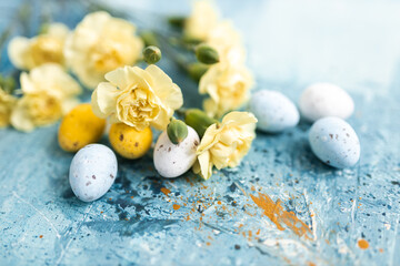 Yellow beautiful flowers and blue and yellow colored easter eggs on a blue picturesque oil painting background close up. Mockups. Layout. Spring pastel background. Easter pastel contemporary backgroun