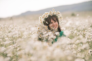 Happy woman in a field of daisies with a wreath of wildflowers on her head. woman in a green dress in a field of white flowers. Charming woman with a bouquet of daisies, tender summer photo