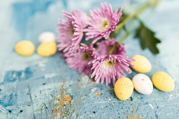 Obraz na płótnie Canvas Pink flowers and yellow and white colored easter eggs on a blue picturesque oil painting background close up. Spring Mockups with pink Gerbers. Layout. Easter pastel background