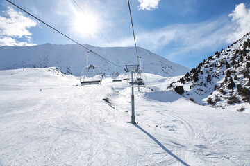 Fototapeta na wymiar Chunkurchak ski resort in Kyrgyzstan. Empty ski lift seats. Mountain slope at sunny winter day, blue sky. Active recreation skiing and snowboarding. Support pillar, Cable car ride.