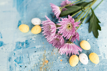 Pink flowers and yellow and white colored easter eggs on a blue picturesque oil painting background...