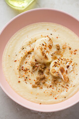 Cream-soup made of roasted cauliflower cabbage and served in a roseate bowl, vertical shot, middle close-up, selective focus