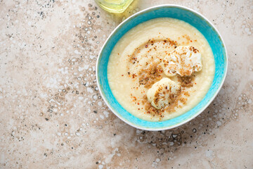 Turquoise bowl with roasted cauliflower cream-soup, above view on a beige granite background, horizontal shot, copy space