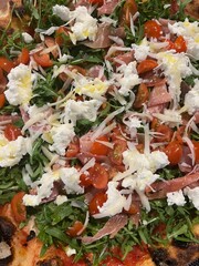 Close up shot from above of the toppings of italian pizza, with tomato, mozzarella, basil, arugula and prosciutto ham.
