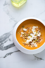 Sweet potato soup topped with feta cheese and chopped pistachios, vertical shot on a white marble background with space, high angle view