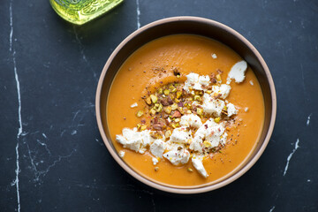 Bowl of sweet potato cream-soup topped with feta and pistachios, horizontal shot on a black marble background, high angle view